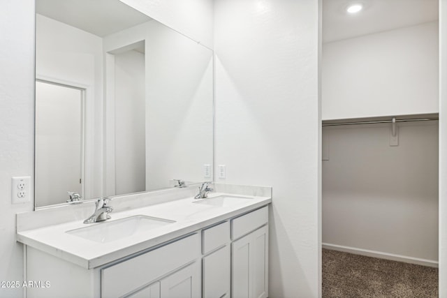 full bathroom with a walk in closet, double vanity, baseboards, and a sink