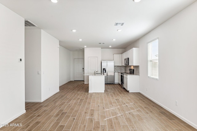 kitchen featuring light wood finished floors, stainless steel appliances, white cabinetry, tasteful backsplash, and open floor plan