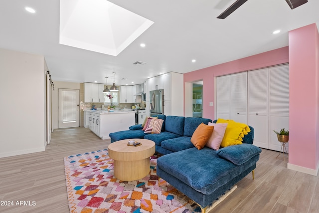 living room with ceiling fan, a barn door, a skylight, and light wood-type flooring