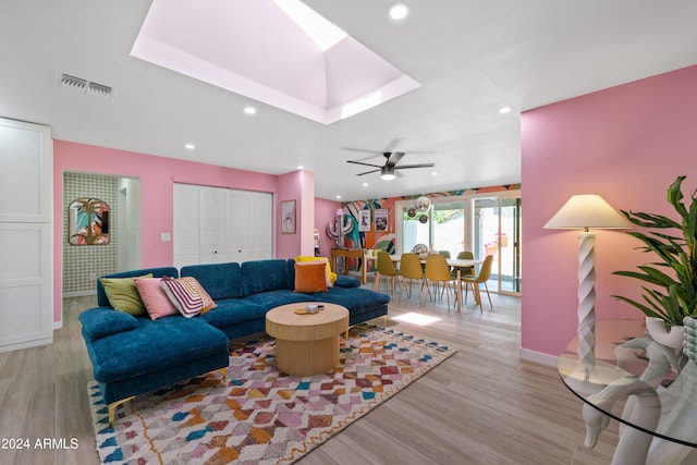 living room with a skylight, ceiling fan, and light wood-type flooring