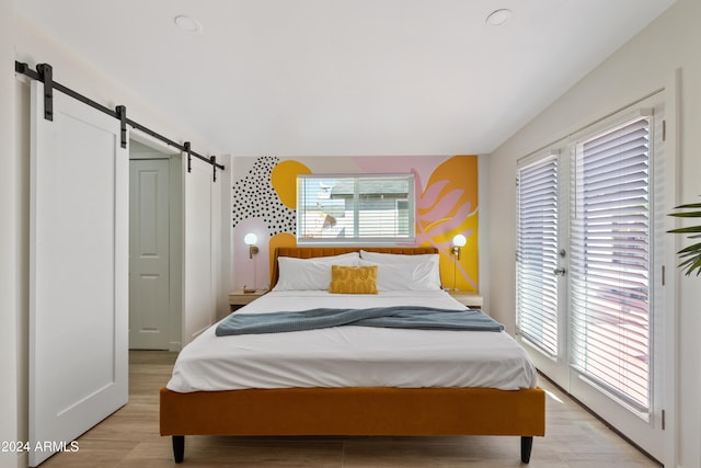 bedroom with a barn door, access to outside, and light hardwood / wood-style floors