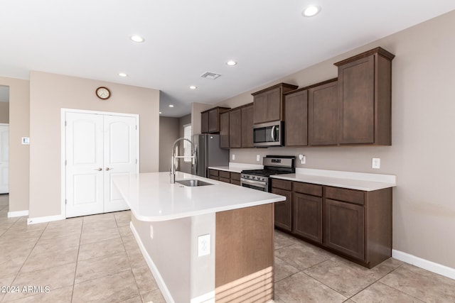 kitchen featuring light tile patterned floors, stainless steel appliances, sink, a center island with sink, and dark brown cabinetry