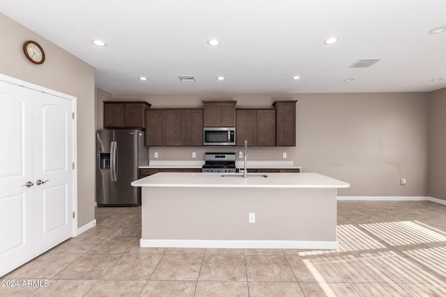 kitchen with stainless steel appliances, sink, dark brown cabinets, light tile patterned flooring, and a kitchen island with sink