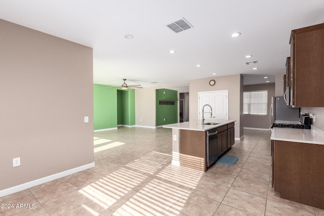 kitchen with light tile patterned floors, appliances with stainless steel finishes, an island with sink, sink, and ceiling fan