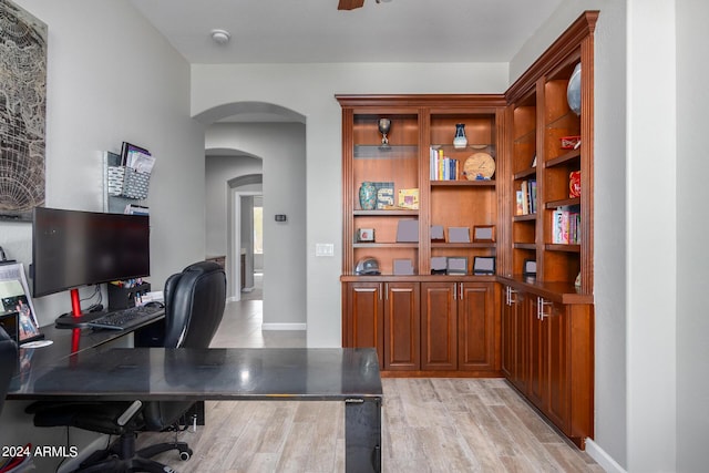 home office featuring arched walkways, light wood-type flooring, and baseboards
