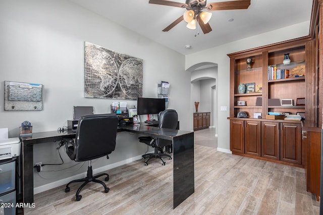home office featuring arched walkways, ceiling fan, light wood-type flooring, and baseboards