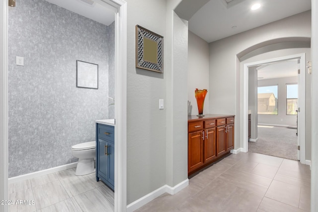 bathroom featuring vanity, baseboards, toilet, tile patterned floors, and wallpapered walls