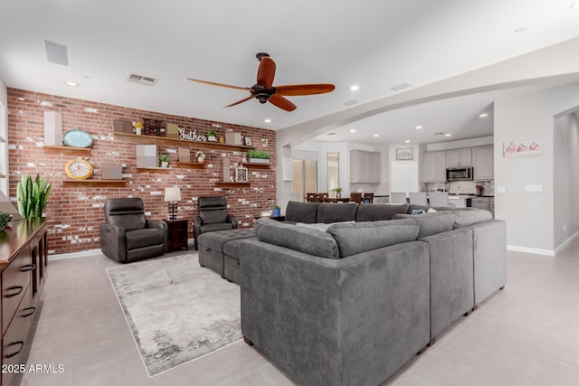 living room with ceiling fan, arched walkways, brick wall, recessed lighting, and baseboards