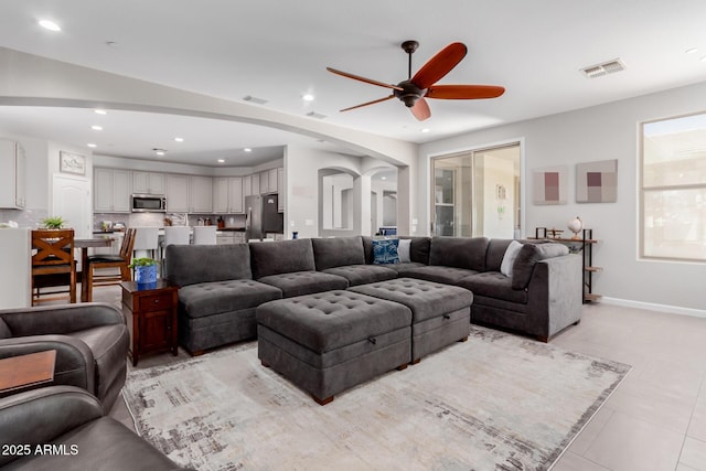 living area featuring arched walkways, a ceiling fan, recessed lighting, light tile patterned flooring, and baseboards