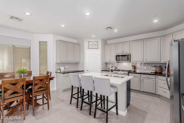 kitchen with stainless steel appliances, gray cabinets, a breakfast bar area, backsplash, and an island with sink
