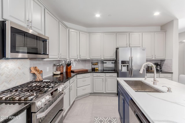 kitchen featuring stainless steel appliances, a sink, tasteful backsplash, dark stone countertops, and recessed lighting