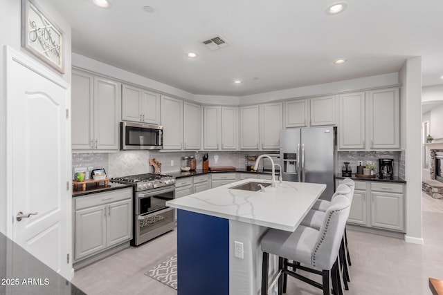 kitchen with appliances with stainless steel finishes, a sink, recessed lighting, decorative backsplash, and a kitchen island with sink