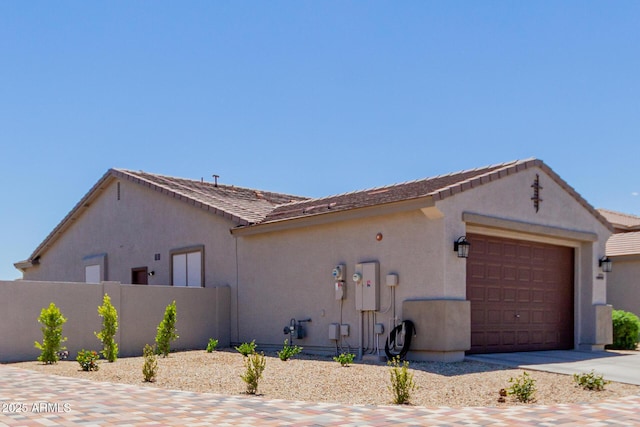 view of property exterior with stucco siding, fence, an attached garage, and driveway