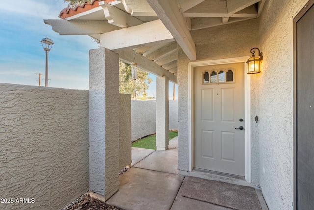 view of exterior entry with stucco siding and fence