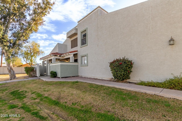 view of side of property with a yard, fence, and stucco siding