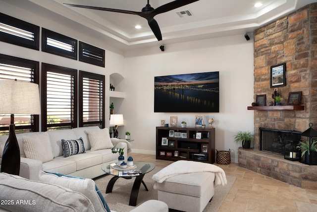 living area featuring stone tile floors, a fireplace, visible vents, and a raised ceiling