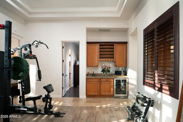 bar featuring visible vents, wine cooler, stainless steel microwave, a tray ceiling, and indoor wet bar