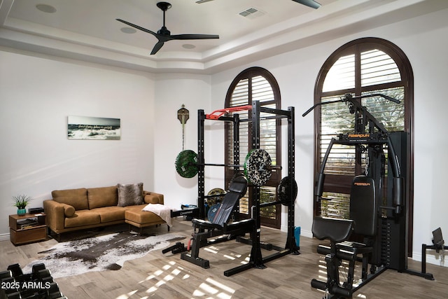 exercise room with a ceiling fan, a raised ceiling, visible vents, and wood finished floors