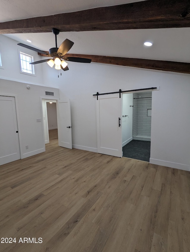 spare room featuring a barn door, ceiling fan, beamed ceiling, and hardwood / wood-style flooring