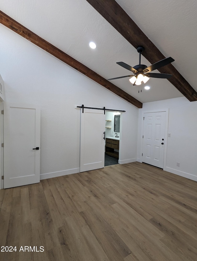 unfurnished living room with wood-type flooring, ceiling fan, sink, a barn door, and lofted ceiling with beams