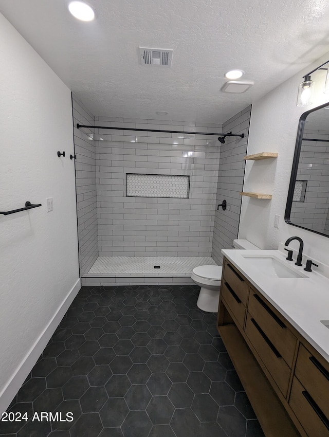 bathroom with tile flooring, tiled shower, toilet, and vanity