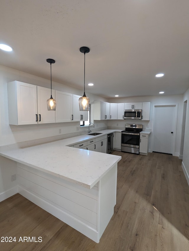 kitchen featuring appliances with stainless steel finishes, kitchen peninsula, hardwood / wood-style flooring, and light stone counters