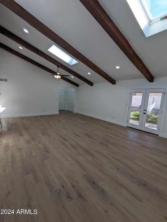 unfurnished living room featuring vaulted ceiling with skylight, ceiling fan, french doors, and dark hardwood / wood-style flooring