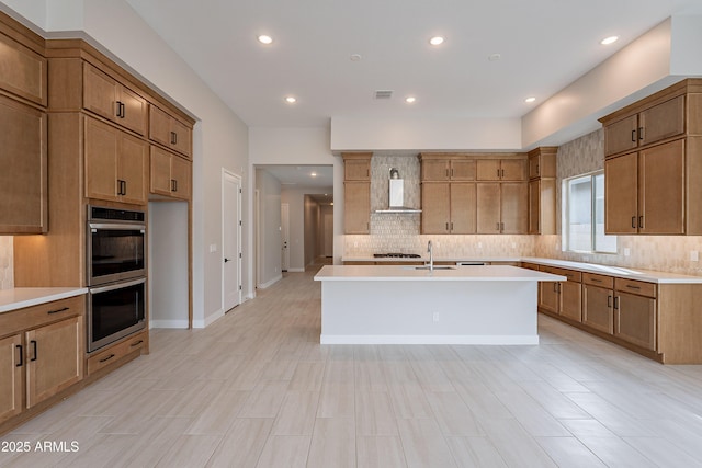 kitchen with sink, wall chimney exhaust hood, stainless steel appliances, decorative backsplash, and a center island with sink