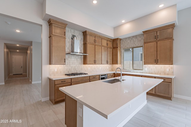 kitchen featuring wall chimney exhaust hood, sink, an island with sink, and stainless steel gas cooktop