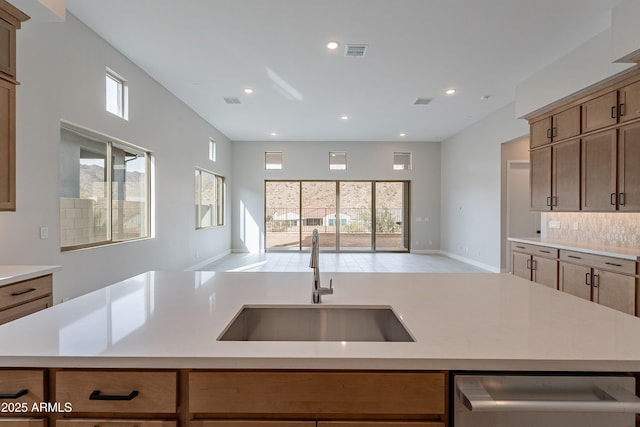 kitchen featuring stainless steel dishwasher, decorative backsplash, sink, and an island with sink