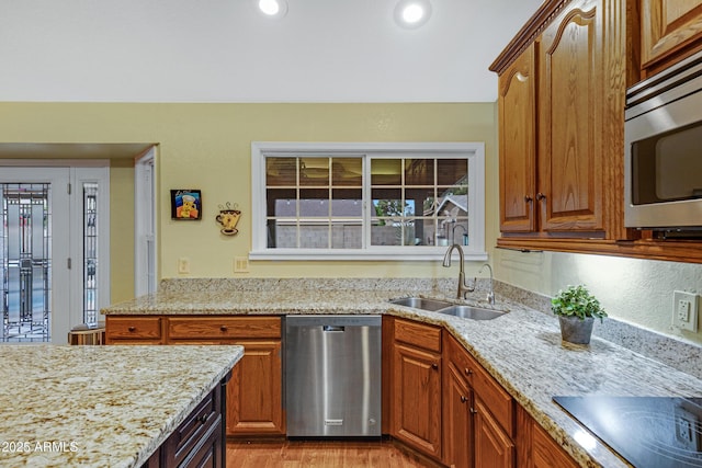 kitchen featuring light wood finished floors, a sink, brown cabinets, light stone counters, and appliances with stainless steel finishes