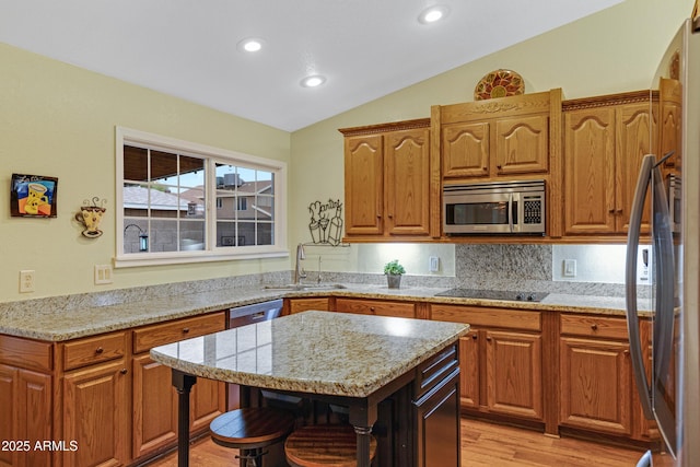 kitchen featuring vaulted ceiling, a sink, light wood-style floors, stainless steel appliances, and a kitchen bar