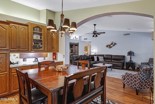 dining space with lofted ceiling, light wood finished floors, visible vents, arched walkways, and ceiling fan with notable chandelier