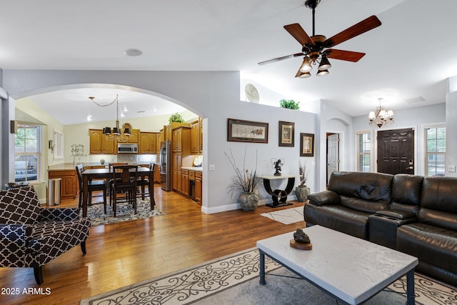 living room with vaulted ceiling, wood finished floors, ceiling fan with notable chandelier, arched walkways, and baseboards