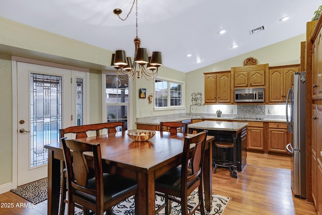 dining room featuring lofted ceiling, visible vents, light wood finished floors, and an inviting chandelier