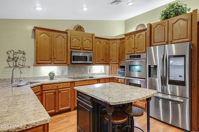 kitchen featuring light wood finished floors, a sink, visible vents, a breakfast bar, and appliances with stainless steel finishes