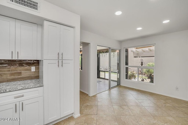 kitchen featuring white cabinets, decorative backsplash, light stone counters, and light tile patterned floors