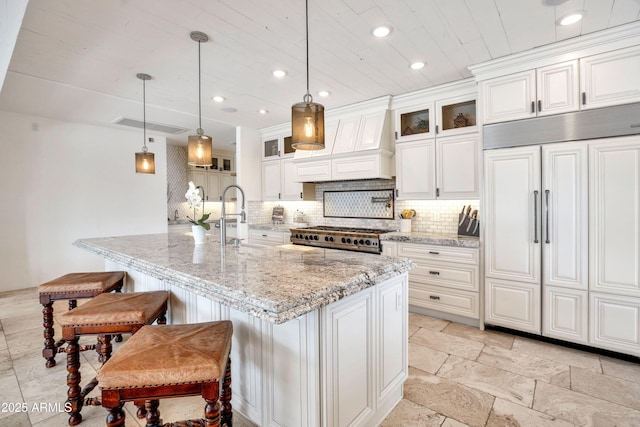 kitchen featuring white cabinetry, an island with sink, light stone countertops, and pendant lighting