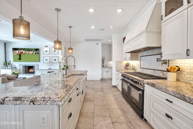 kitchen with range with two ovens, white cabinetry, pendant lighting, and a large island with sink