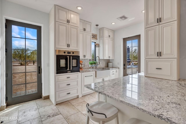 kitchen with a kitchen bar, light stone countertops, pendant lighting, oven, and decorative backsplash