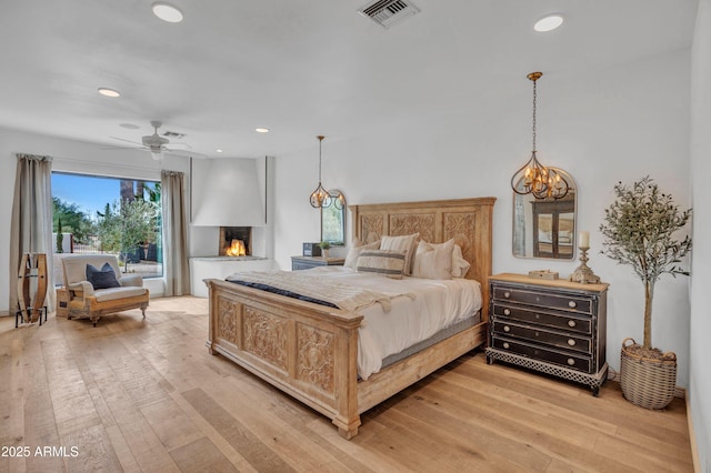 bedroom featuring a multi sided fireplace, ceiling fan, and light hardwood / wood-style floors