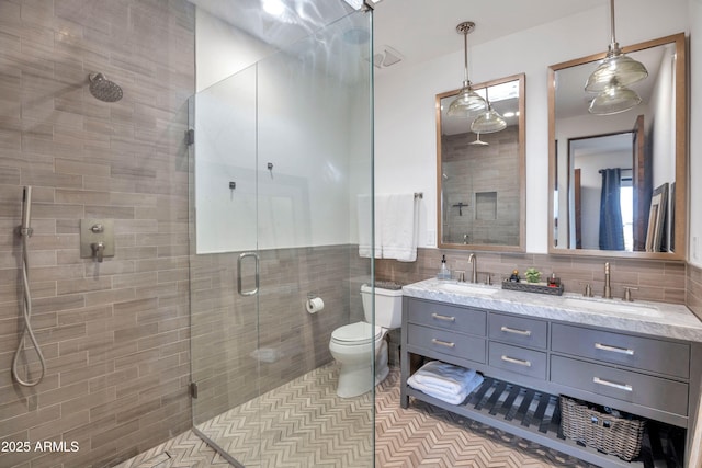 bathroom with toilet, a shower with shower door, tile walls, vanity, and tile patterned flooring