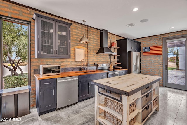 kitchen with wall chimney exhaust hood, sink, wooden counters, pendant lighting, and stainless steel appliances