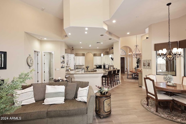 living room with an inviting chandelier, light hardwood / wood-style flooring, and a towering ceiling