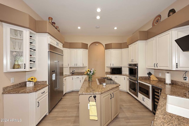 kitchen with a kitchen island, built in appliances, dark stone countertops, white cabinetry, and light hardwood / wood-style floors