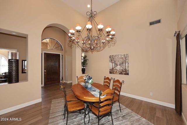 dining area featuring a towering ceiling, an inviting chandelier, and dark wood-type flooring