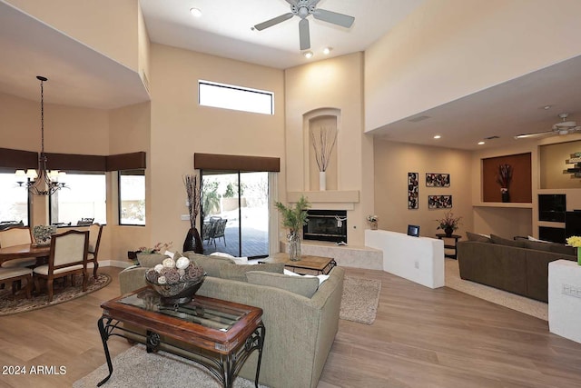 living room featuring a towering ceiling, a large fireplace, ceiling fan with notable chandelier, and light hardwood / wood-style floors