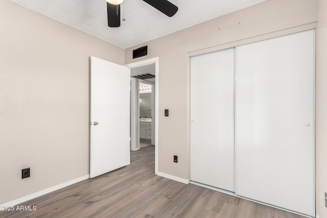 unfurnished bedroom with light wood-style floors, a textured ceiling, baseboards, and a closet