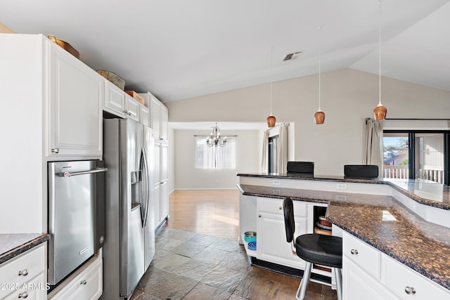 kitchen with lofted ceiling, white cabinets, stainless steel fridge with ice dispenser, decorative light fixtures, and dark stone counters