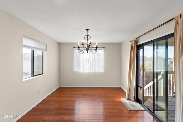 empty room featuring a wealth of natural light, dark wood-type flooring, and a chandelier